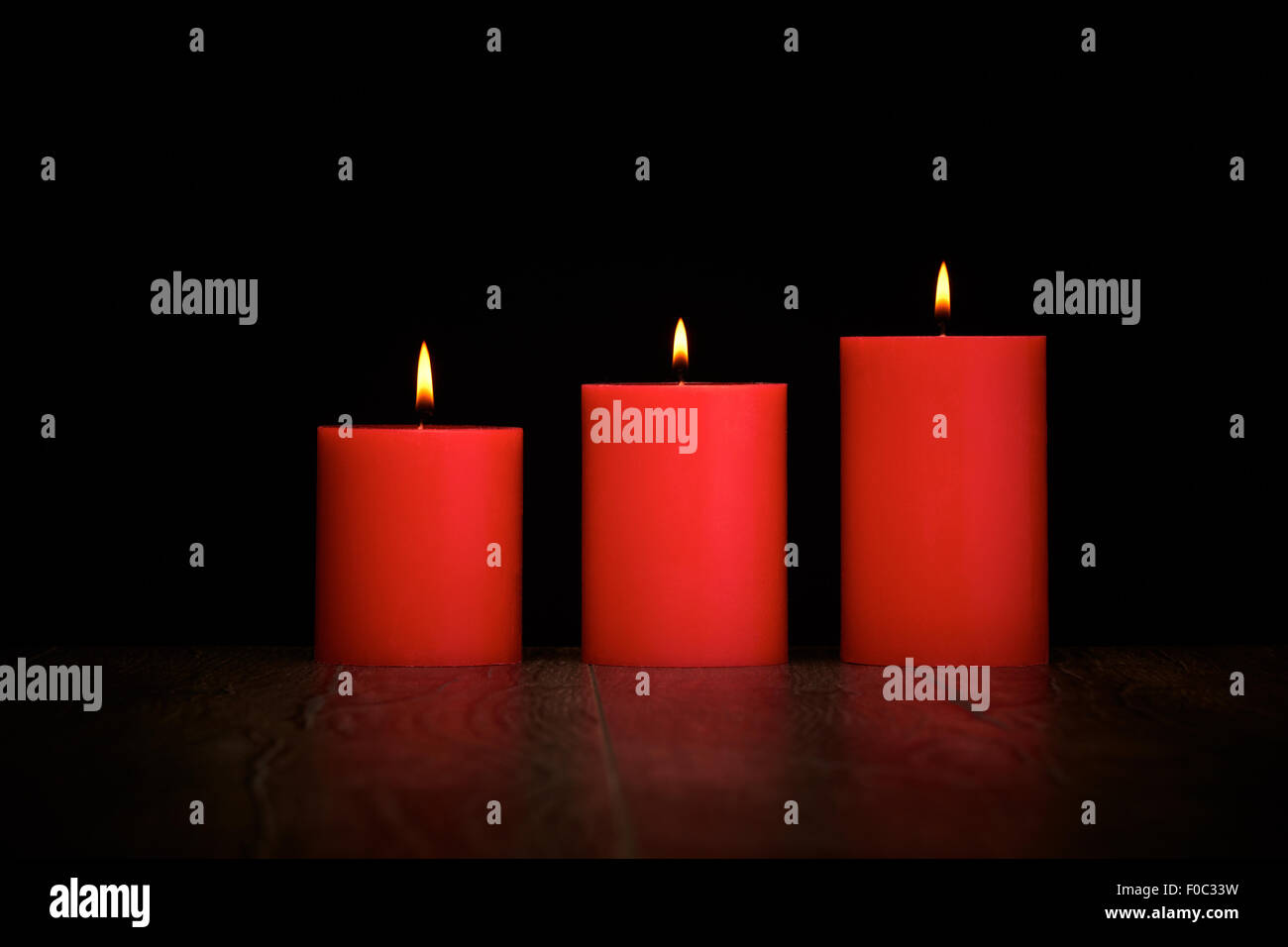 Rote Kerzen auf einem dunklen Holzboden mit schwarzem Hintergrund. Stockfoto