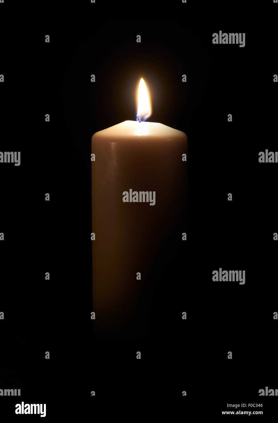 Beleuchtete weiße Kerze auf einem dunklen Holzboden mit schwarzem Hintergrund. Stockfoto