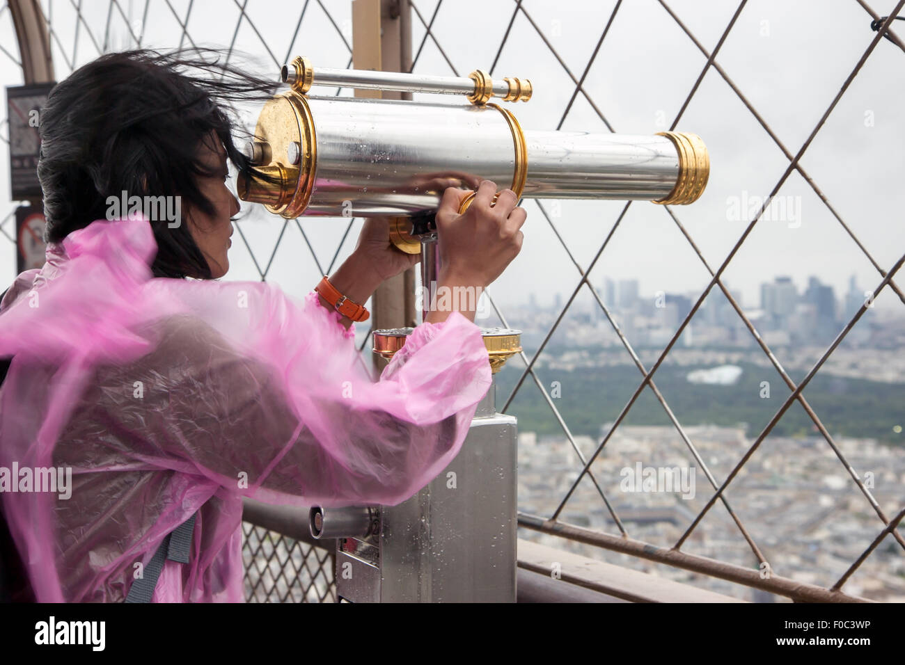 Frau im Regenmantel schauen durch ein Fernglas in der Nähe von Eiffelturm Stockfoto