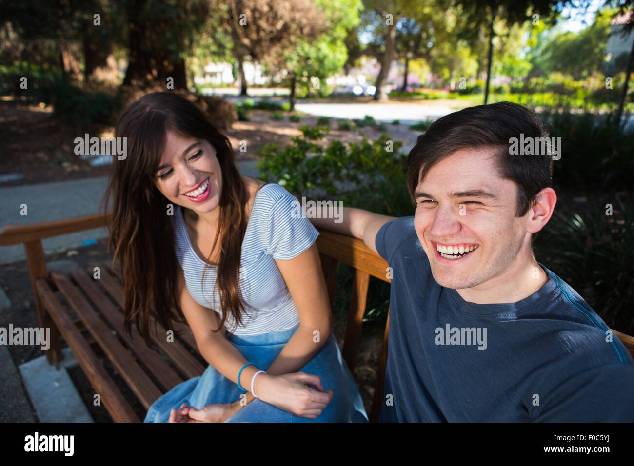 Junges Paar lachend auf Parkbank Stockfoto