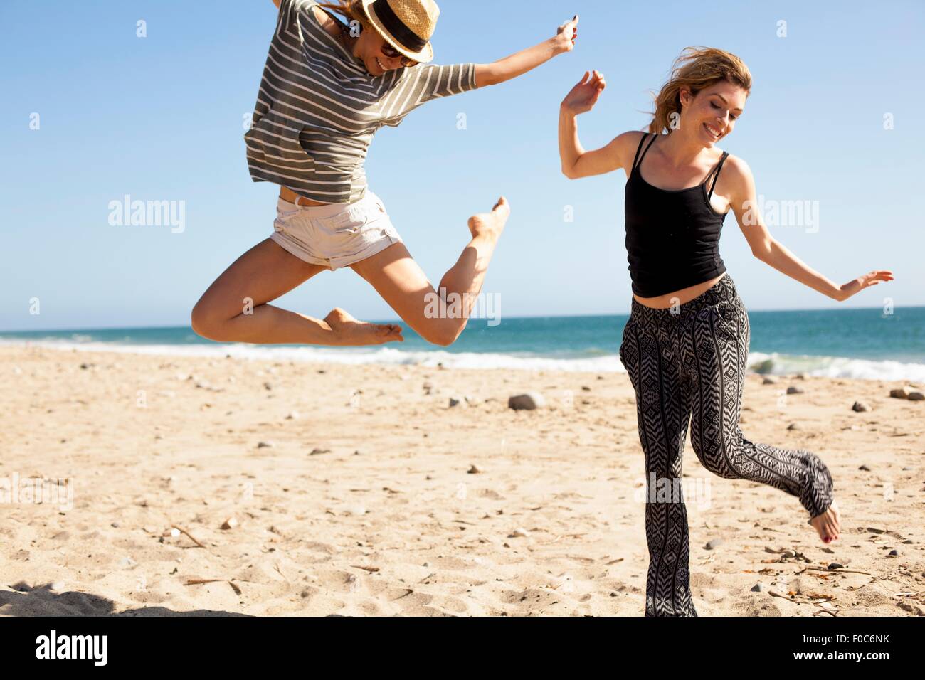 Freundinnen springen in der Luft am Strand von Malibu, Kalifornien, USA Stockfoto