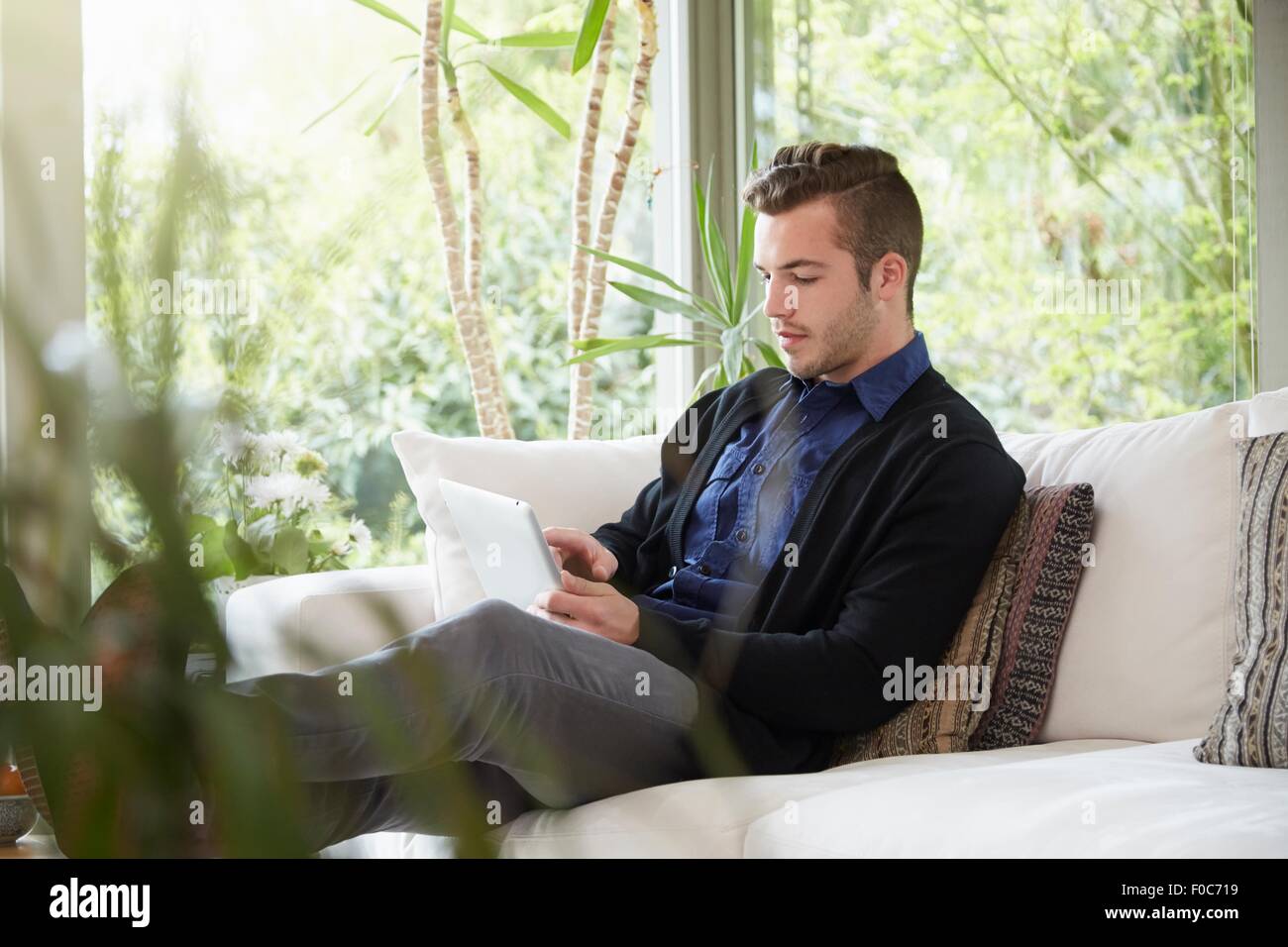 Mann auf Sofa mit Füßen auf der Suche um digital-Tablette Stockfoto