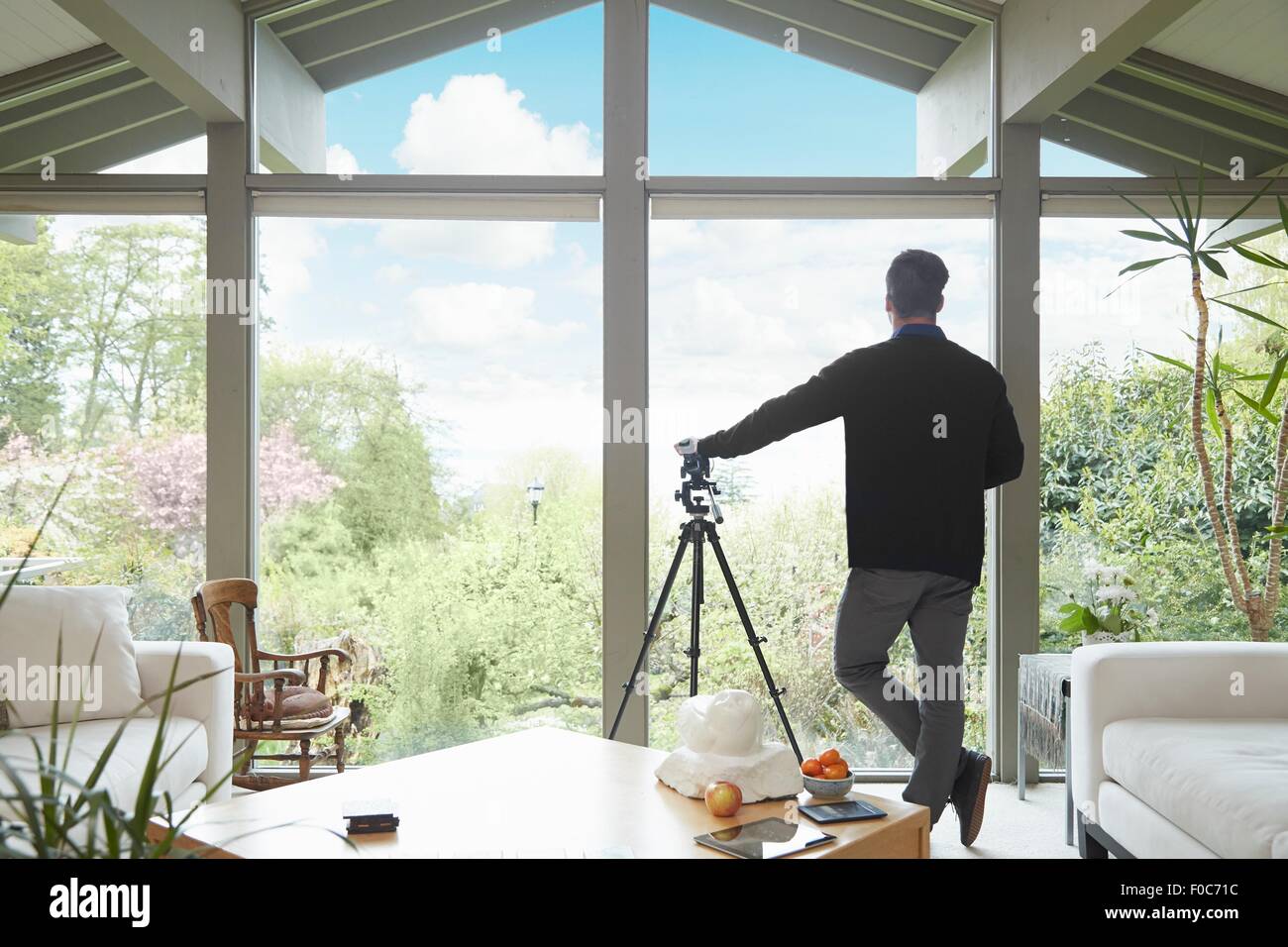 Rückansicht des Mannes stützte sich auf Teleskop Blick aus Fenster bewundern Sie malerische Garten Stockfoto