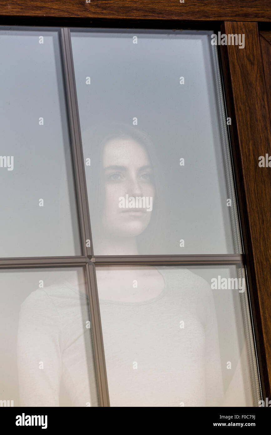 Nachdenkliche junge Frau Blick durch Fenster Stockfoto