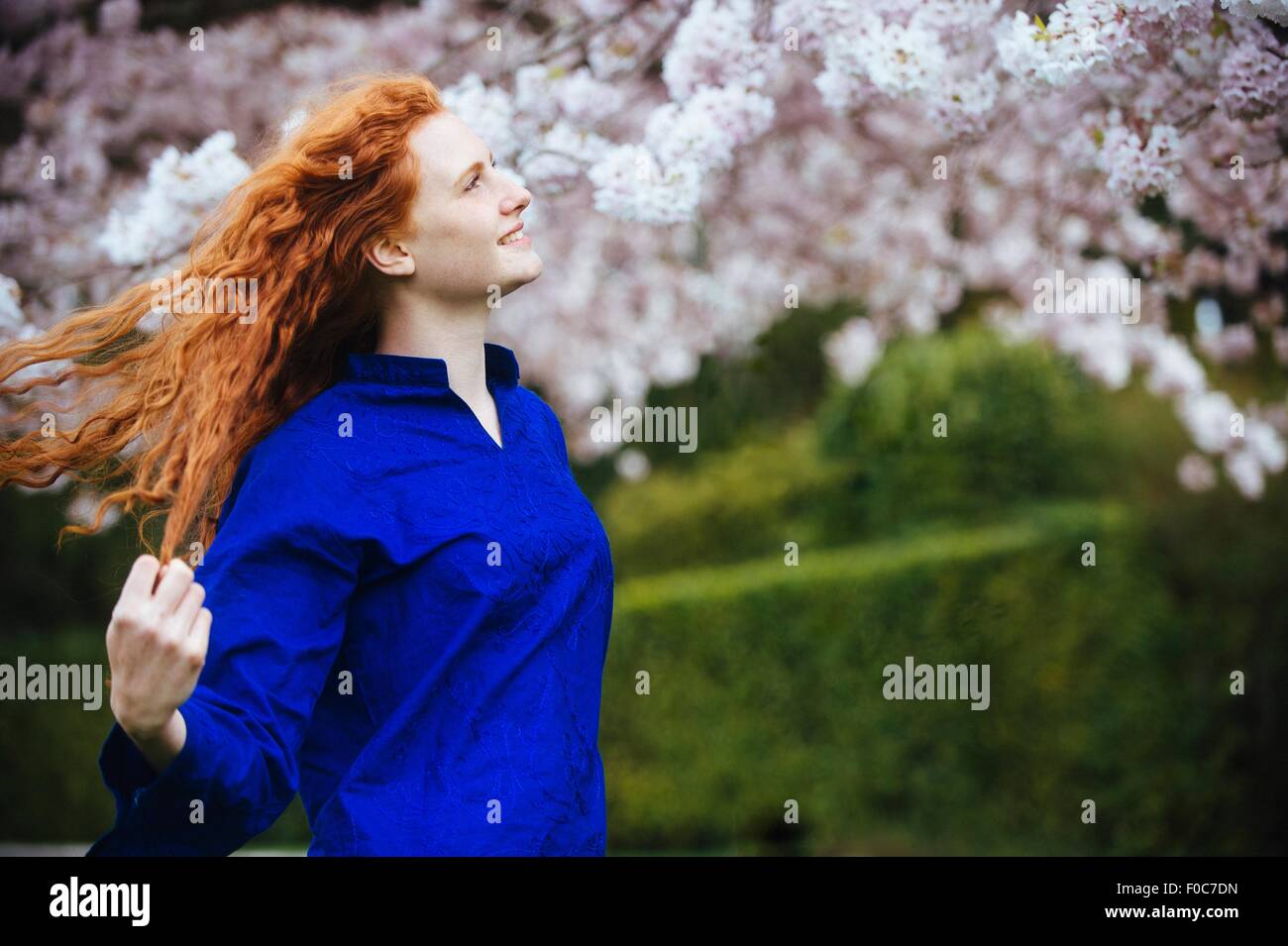 Porträt der jungen Frau mit langen gewellten roten Haaren im Frühlingspark Stockfoto