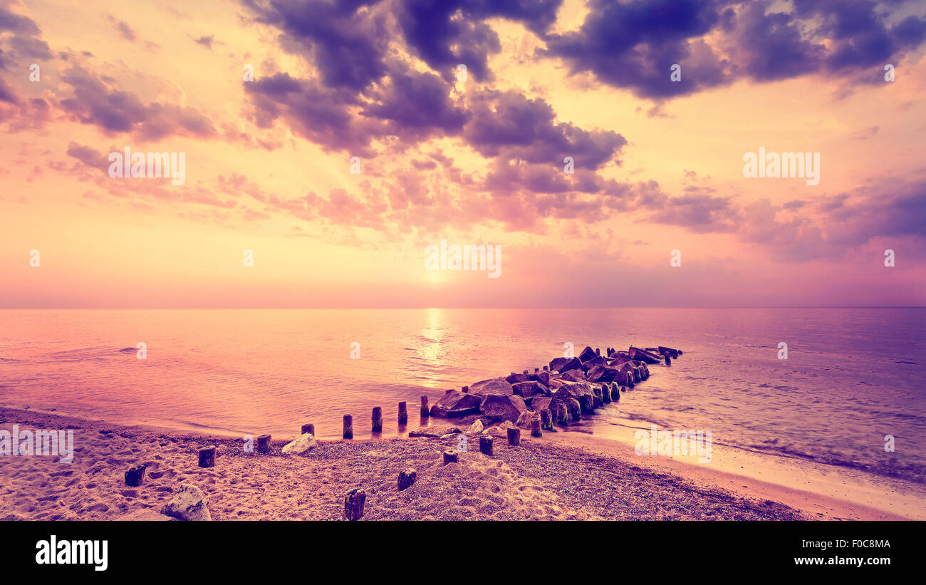 Jahrgang gefiltert lila Sonnenuntergang über Strand und felsigen Pier. Stockfoto