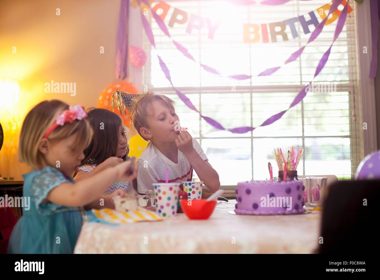 Drei Kinder sitzen am Tisch essen lila Geburtstagstorte Stockfoto