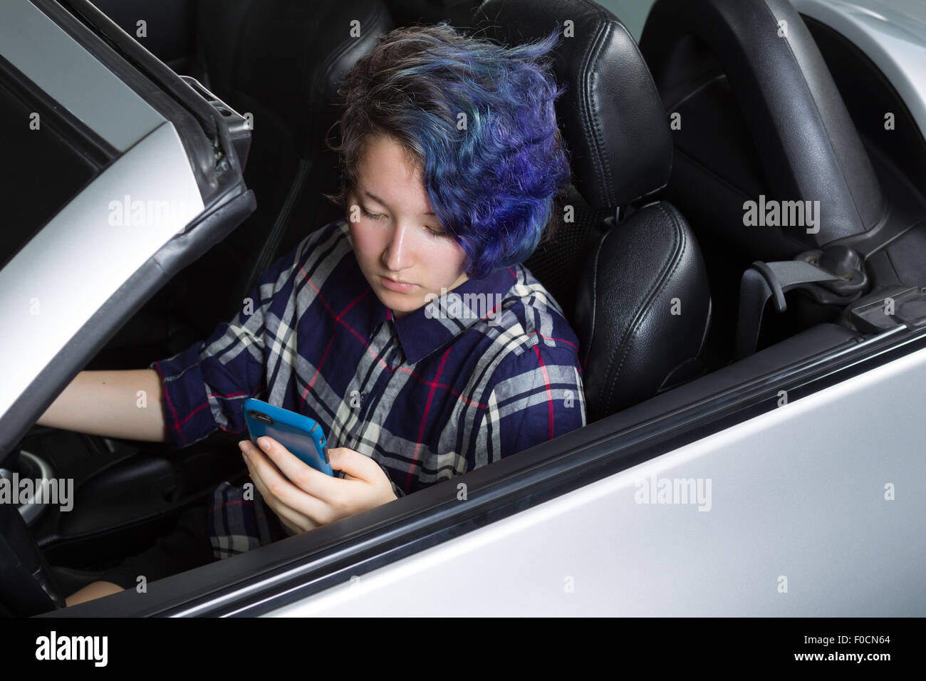 Teenager-Mädchen blickte auf Handy SMS im Fahrersitz des Autos. Konzentrieren Sie sich auf ihr Gesicht. Gemischte asiatische und kaukasische Mädchen. Stockfoto