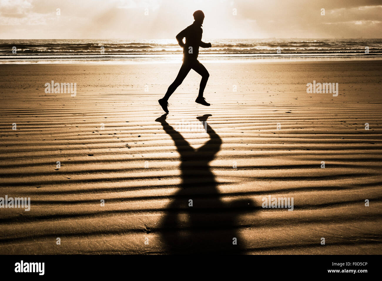 Mann läuft am Strand bei Sonnenaufgang gegen aufgehende Sonne Stockfoto