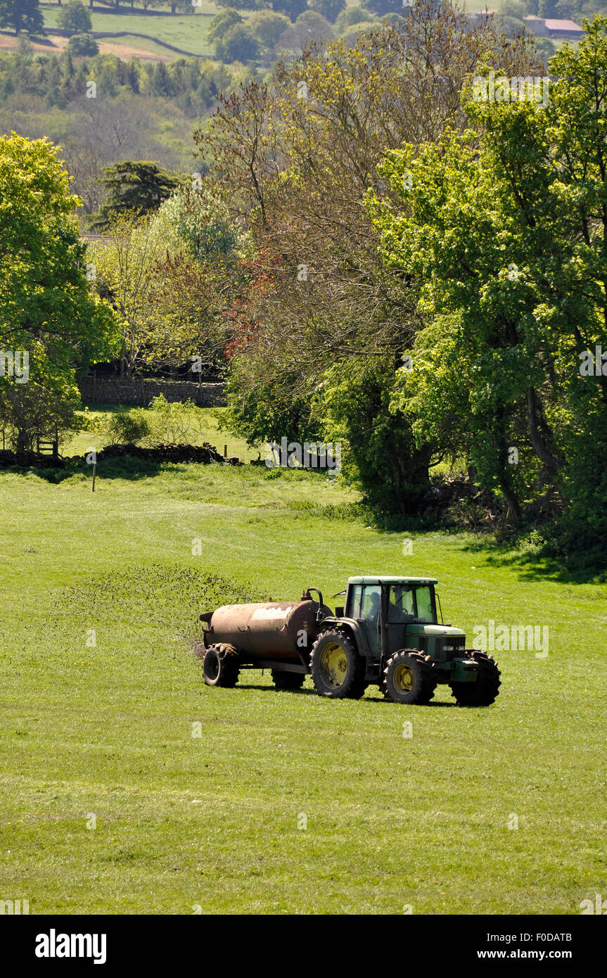 Landwirt fährt Traktor mit Miststreuer über Feld Stockfoto
