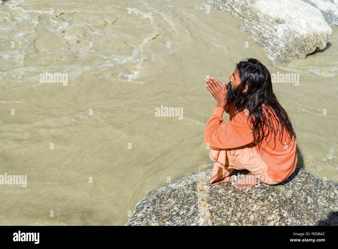 Ein Sadhu, heiliger Mann, sitzt und beten auf einem Felsen am Gaumukh, die Hauptquelle des heiligen Flusses Ganges, Gangotri, Uttarakhand Stockfoto