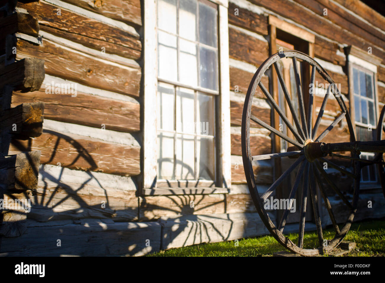 Am frühen Morgensonnenlicht werfen einen Schatten von einem großen Holzwagen-Rad auf die Seite von einem Blockhaus in Nevada City Ghost Town Stockfoto