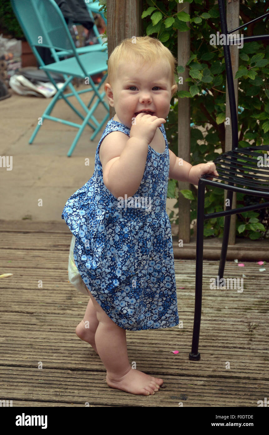 Ein zehn Monate altes baby stehen, stützte sich mit einem Gartenstuhl. Stockfoto