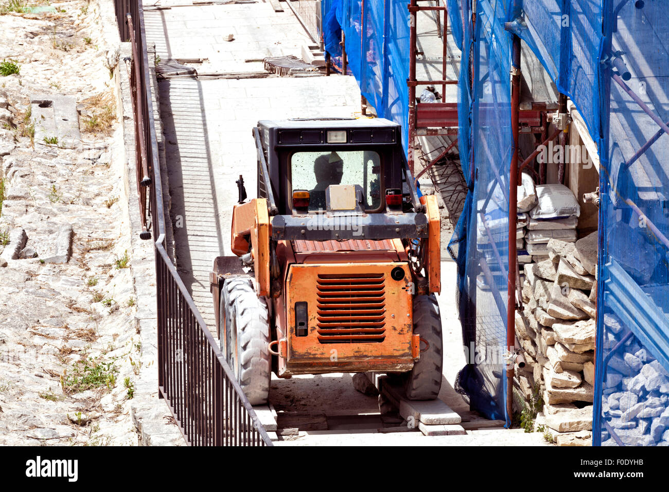 Kleine orange heben Fahrzeug bergauf auf einem Gebäude Baustelle, voll von Zementsäcken, Steinplatten, mit Gerüst Stockfoto