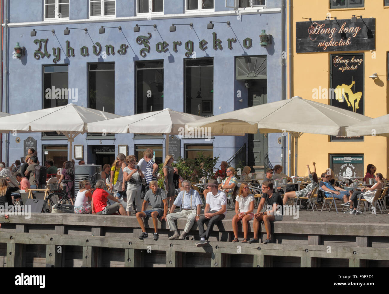 In gemütlichem Ambiente im bezaubernden Nyhavn treffen sich die Menschen und unterhalten sich über einen Drink in der Sonne. Viele Leute sitzen gerne auf dem Kai unter den alten Schiffen. Hygge. Stockfoto