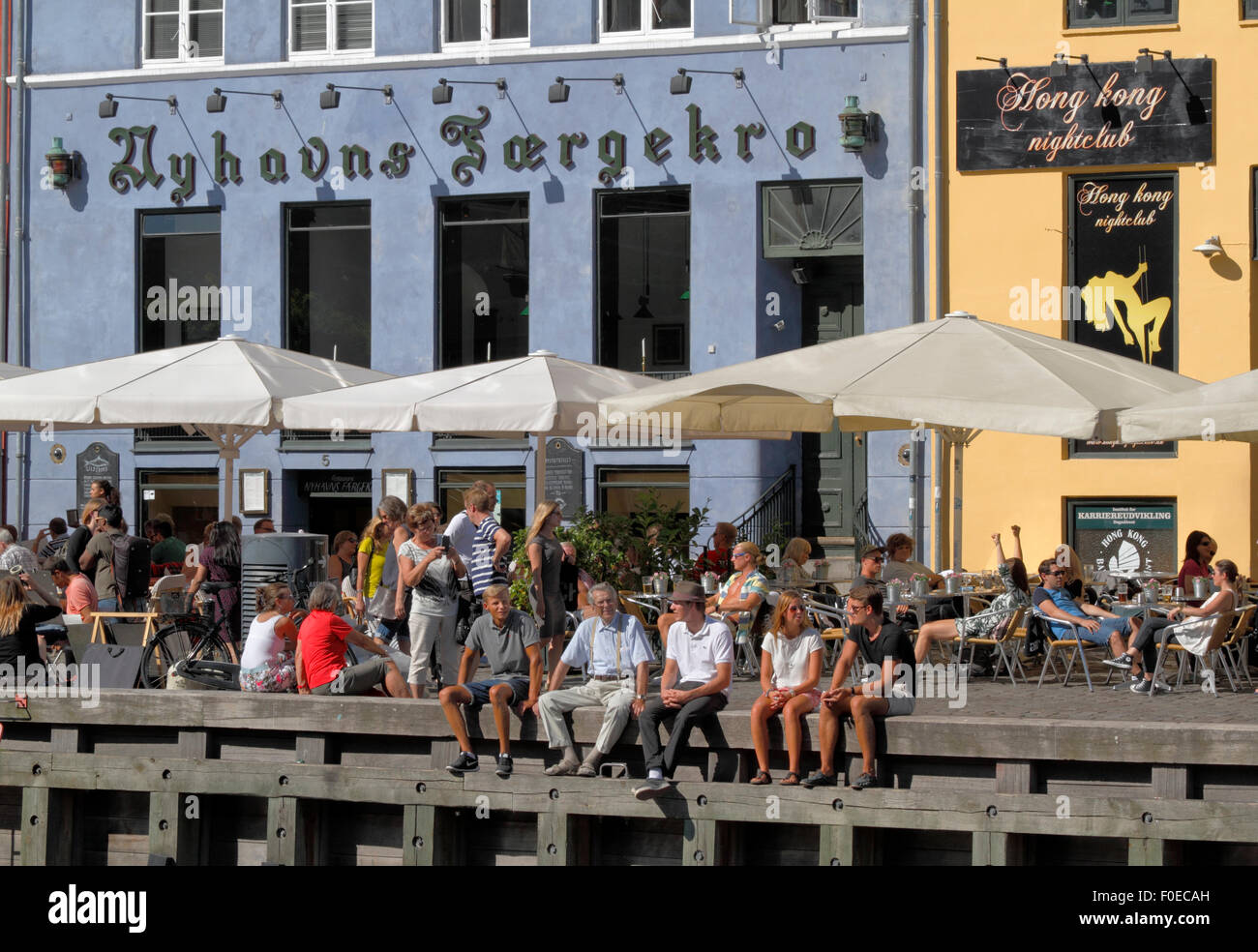 Im gemütlichen Ambiente des bezaubernden Nyhavn treffen sich die Menschen und unterhalten sich über einen Drink in der Sonne. Viele sitzen lieber auf der Wharf unter den alten Schiffen. Hygge. Stockfoto