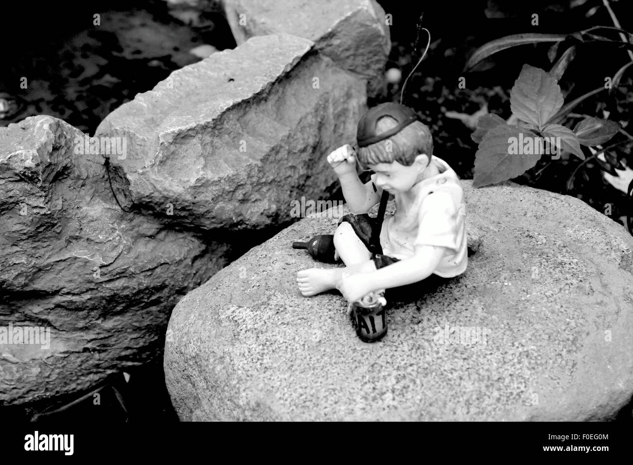 Figur eines jungen ohne Schuhe tragen eine Baseballmütze sitzt auf einem großen Felsen Stockfoto