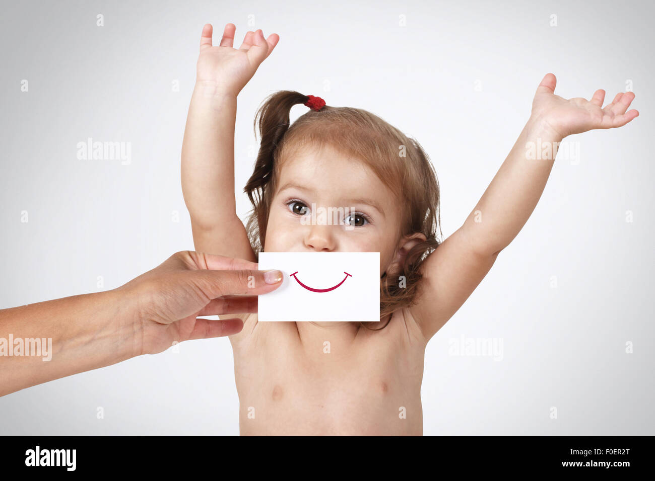 Glücklich fröhliche Babymädchen versteckt ihr Gesicht mit der hand mit Lächeln auf Papier auf grauem Hintergrund gezeichnet Stockfoto