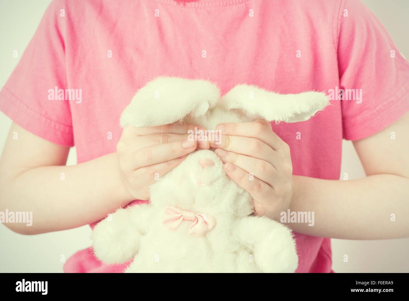 Kleines Mädchen Stofftier Tier mit den Händen zu halten. Sie deckt die Augen des Kaninchens Spielzeug. Konzeptbild von Kindheit Unsicherheit, Unschuld und Verletzlichkeit. Stockfoto