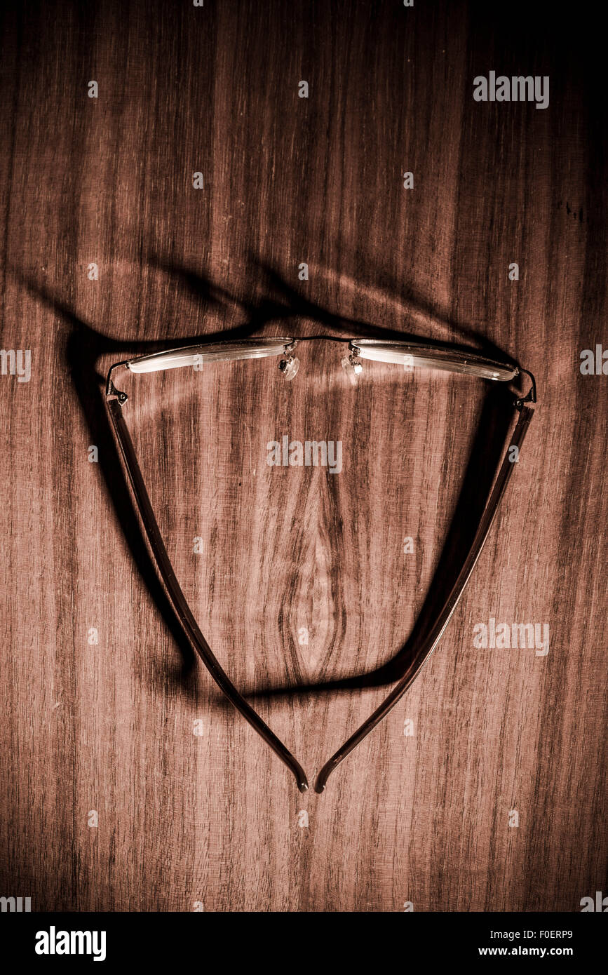 Brillen auf Holztisch mit Schatten der Gläser auf der Oberfläche. Stockfoto