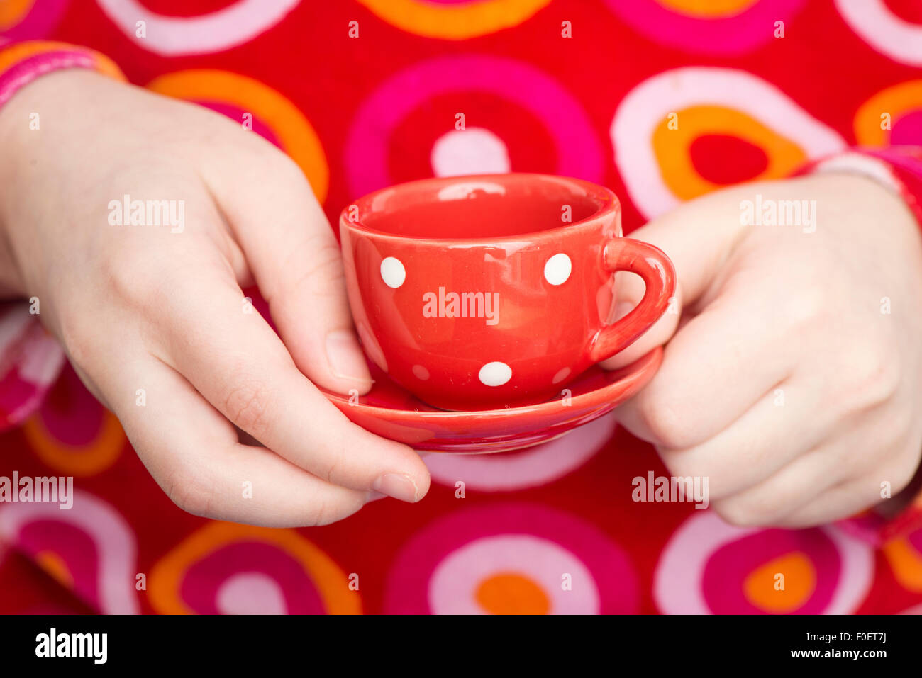 Kleines Mädchen hält gepunktete Teetasse spielen Teaparty. Nahaufnahme der Hände des Kindes. Das Bild zeigt einen entzückenden Moment der unschuldigen Kindheit spielen. Stockfoto