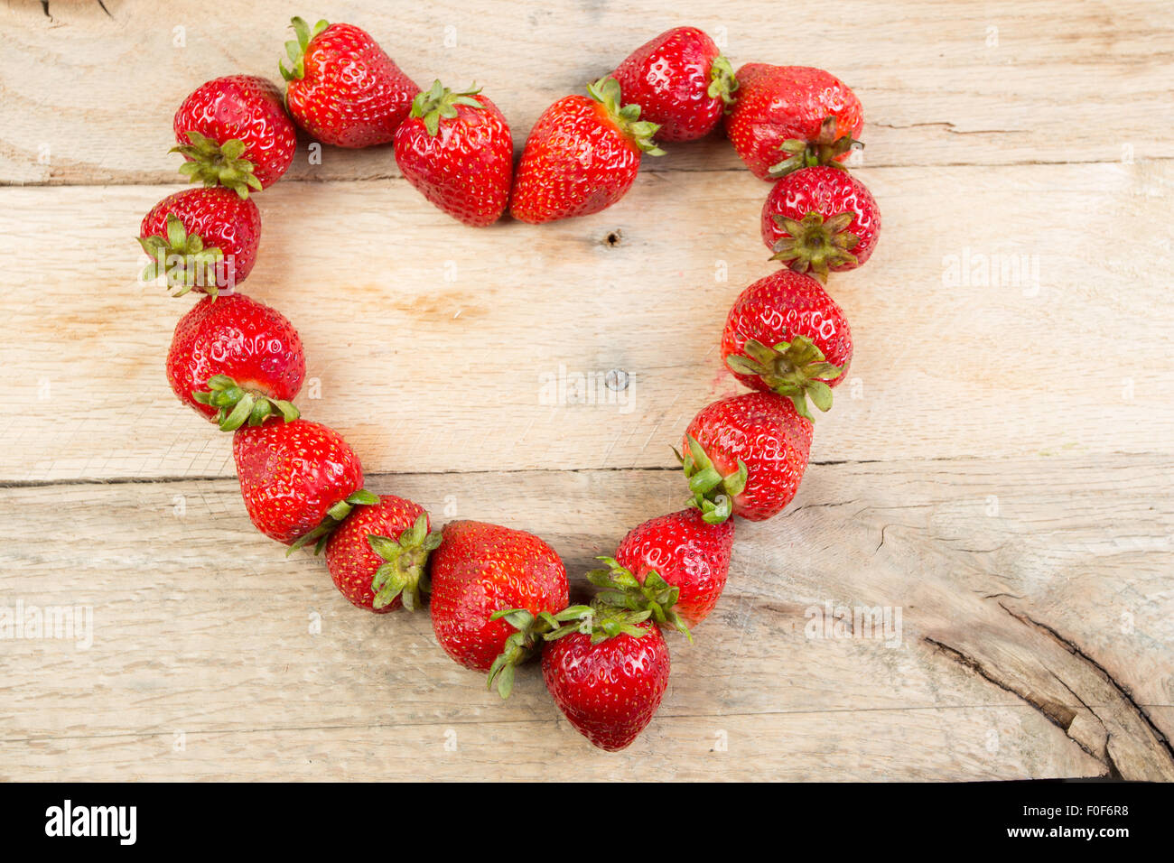 Erdbeeren in Form eines Herzens auf einem rustikalen Holz Hintergrund positioniert. Stockfoto