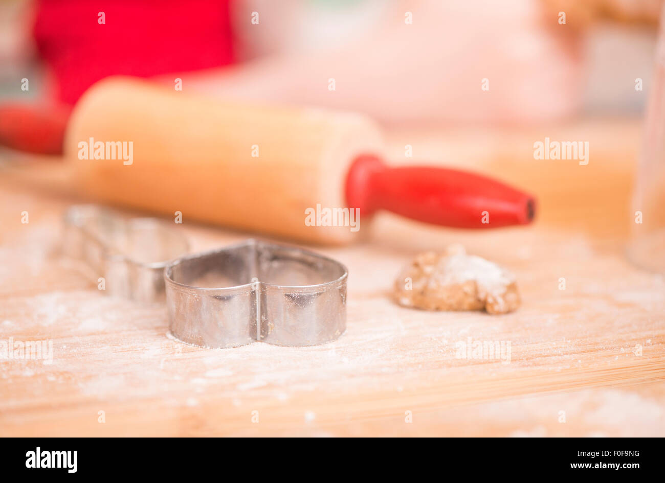 Ausstecher, Lebkuchen-Cookie-Teig und Nudelholz auf Holzbrett. Junges Mädchen im Hintergrund. Stockfoto