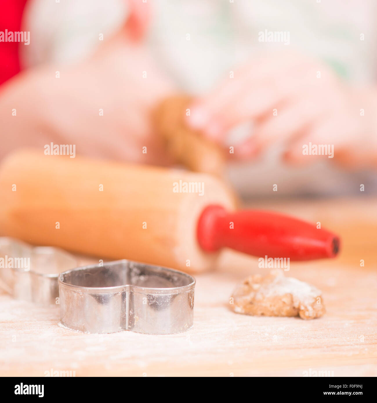 Ausstecher, Lebkuchen-Cookie-Teig und Nudelholz auf Holzbrett. Junges Mädchen im Hintergrund. Stockfoto