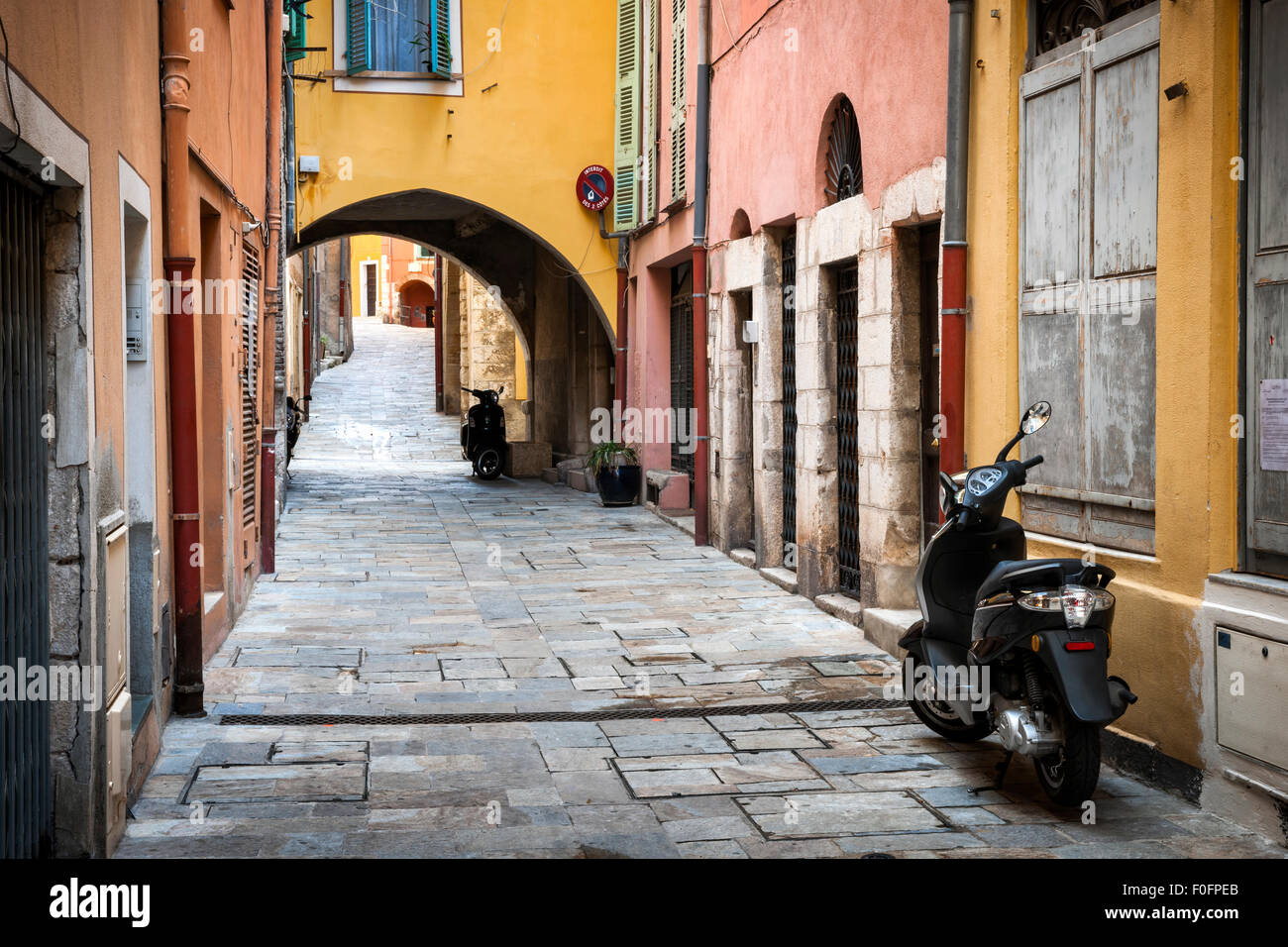 Schmale gepflasterte Straße mit farbenfrohen Gebäuden und geparkten Roller in der mittelalterlichen Stadt Villefranche-Sur-Mer an der Côte d ' Azur, Stockfoto