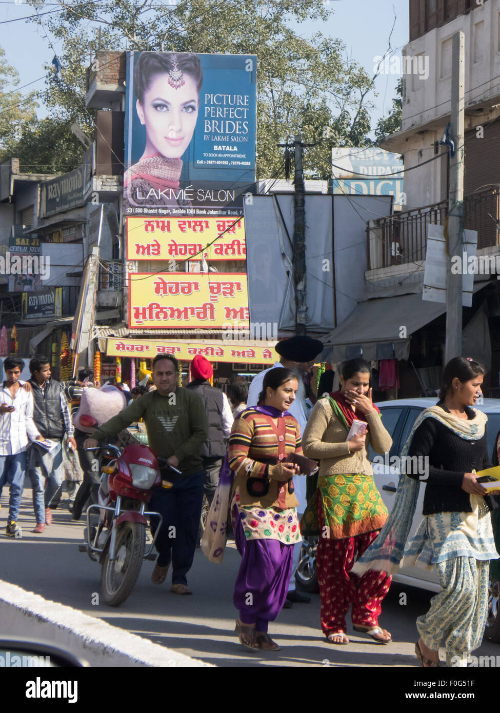Amritsar, Punjab, Indien. Straßenbild; Fußgänger, die unten eine Werbung für "Bild perfekte Bräute" in englischer Sprache mit einem roten und gelben Schild in Punjabi unten vorbei. Stockfoto