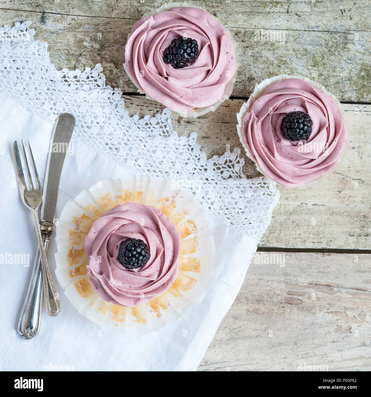 Ansicht von oben drei Blackberry Cupcakes auf rustikalen Holztisch mit geschnürten Tischdecke und Vintage Besteck Stockfoto