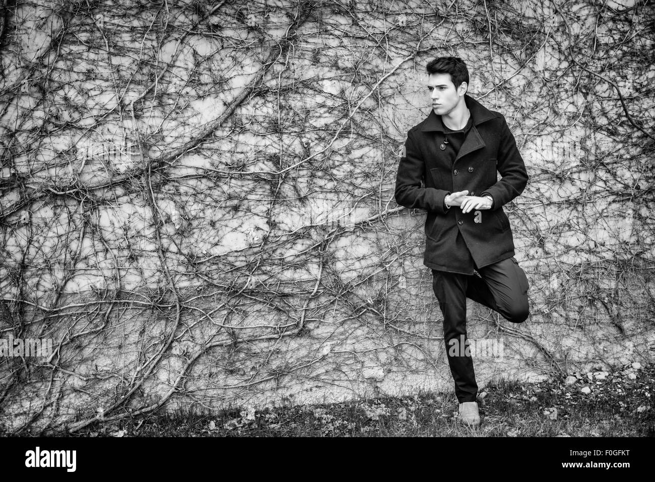 Hübscher ernst junger Mann stehend gegen Pflanzenwand bedeckt tragen Winterkleidung Stockfoto