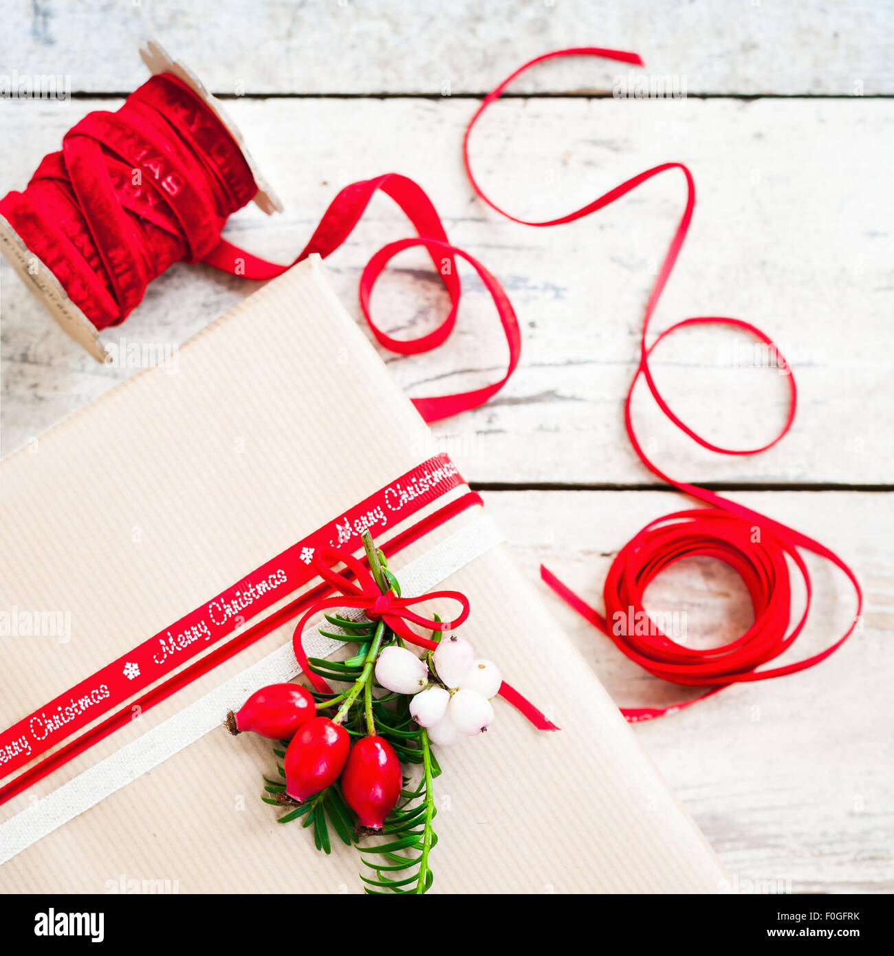 einfaches Geschenk mit braunem Papier eingewickelt und mit rotem Band und Beeren dekoriert Stockfoto