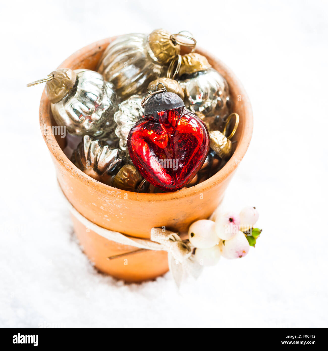 ein kleine Terrakotta-Topf gefüllt mit Christbaumkugeln und dekoriert mit einem Zweig von Snowberry, auf dem Schnee, Stockfoto