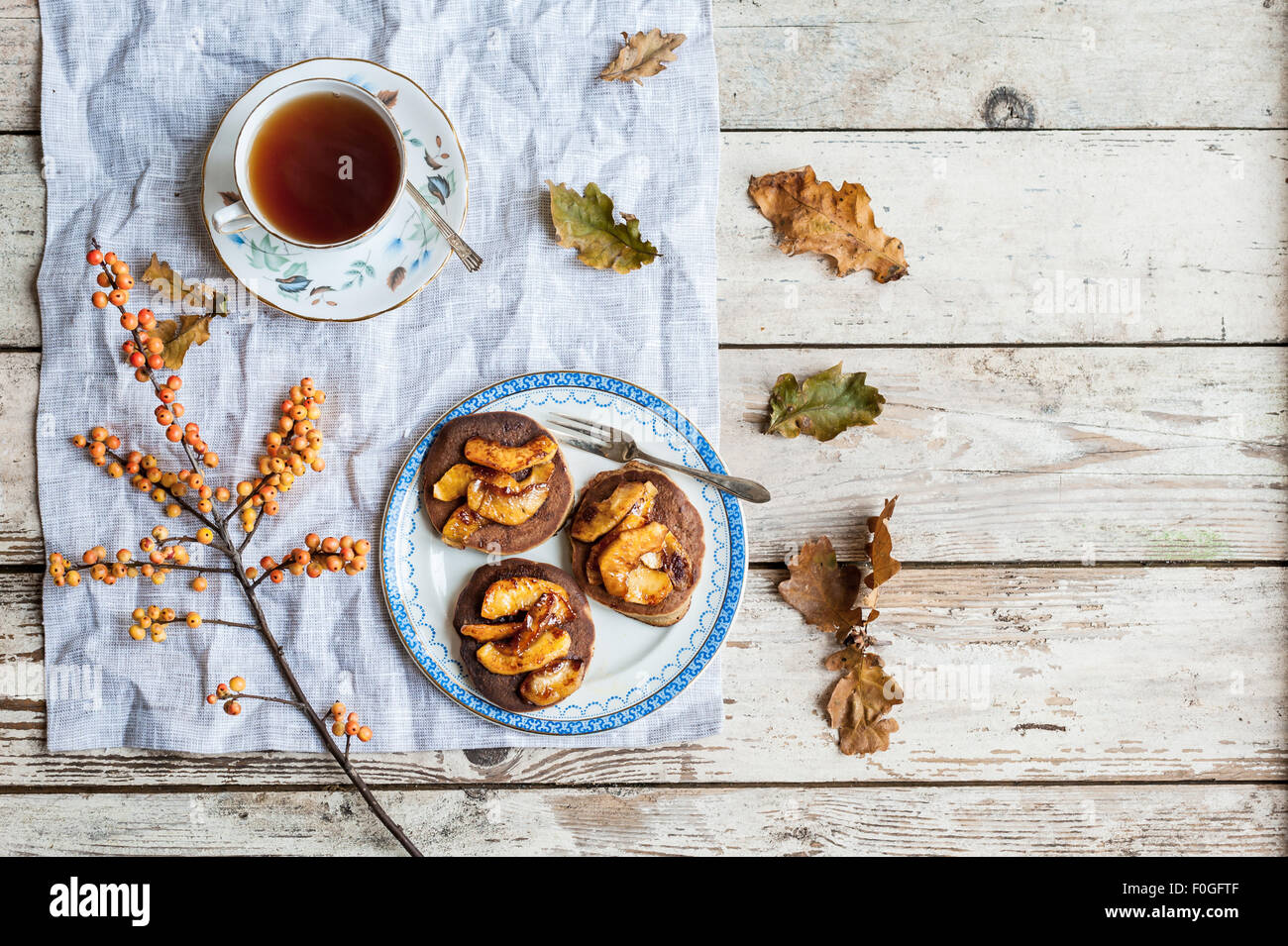 Pfannkuchen mit karamellisierten Äpfeln auf Vintage Teller mit Tee in Vintage Teetasse, Eichenlaub und Ilex Beeren Stockfoto
