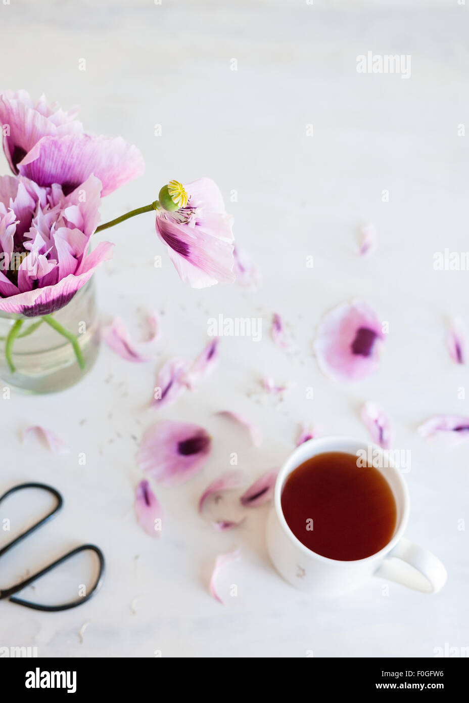 Rosa Mohnblumen mit Becher Tee und Schere Stockfoto