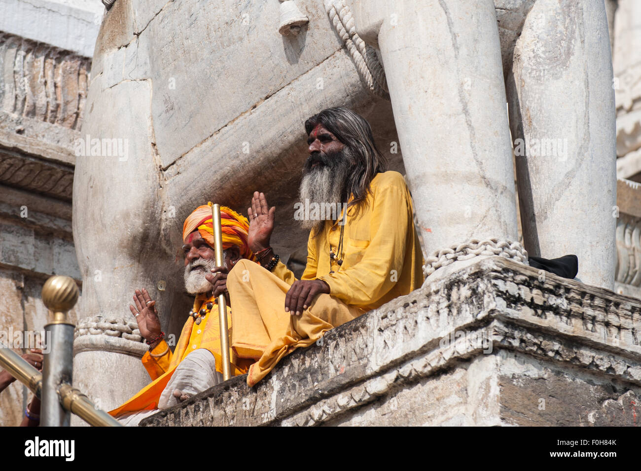 Udaipur, Indien. Hindu Sadhu heilige Männer gekleidet in Safran Roben sitzen unter der Statue eines Elefanten am Eingang zum 17. Jahrhundert Jagdish Tempel mit ihren Händen in Gruß erhoben. Stockfoto