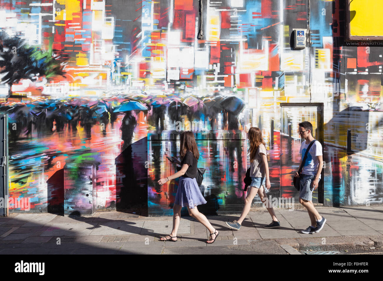 Junge Menschen gehen vorbei an einer bunt bemalten Wand in Camden Town, London. Stockfoto