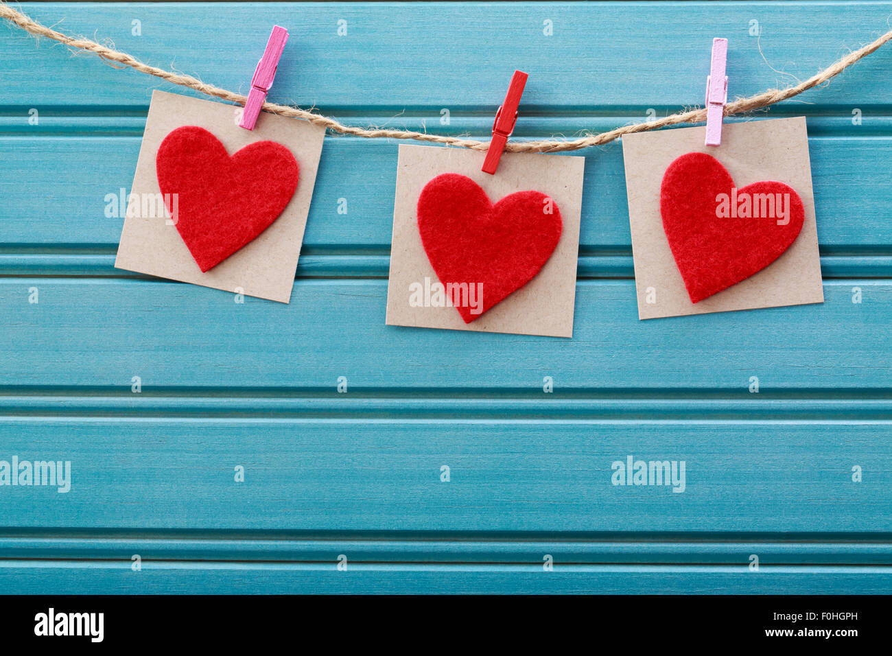 Handgefertigte Filz Herzen hängen mit Wäscheklammern über blaue Holzbrett Stockfoto