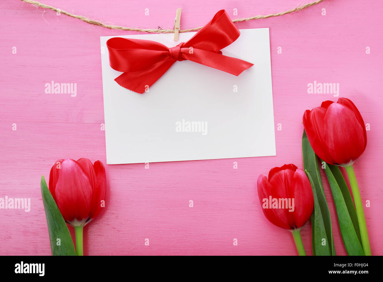 Textkarte mit Wäscheklammern über rote Tulpen und rosa Holzbrett hängen Stockfoto