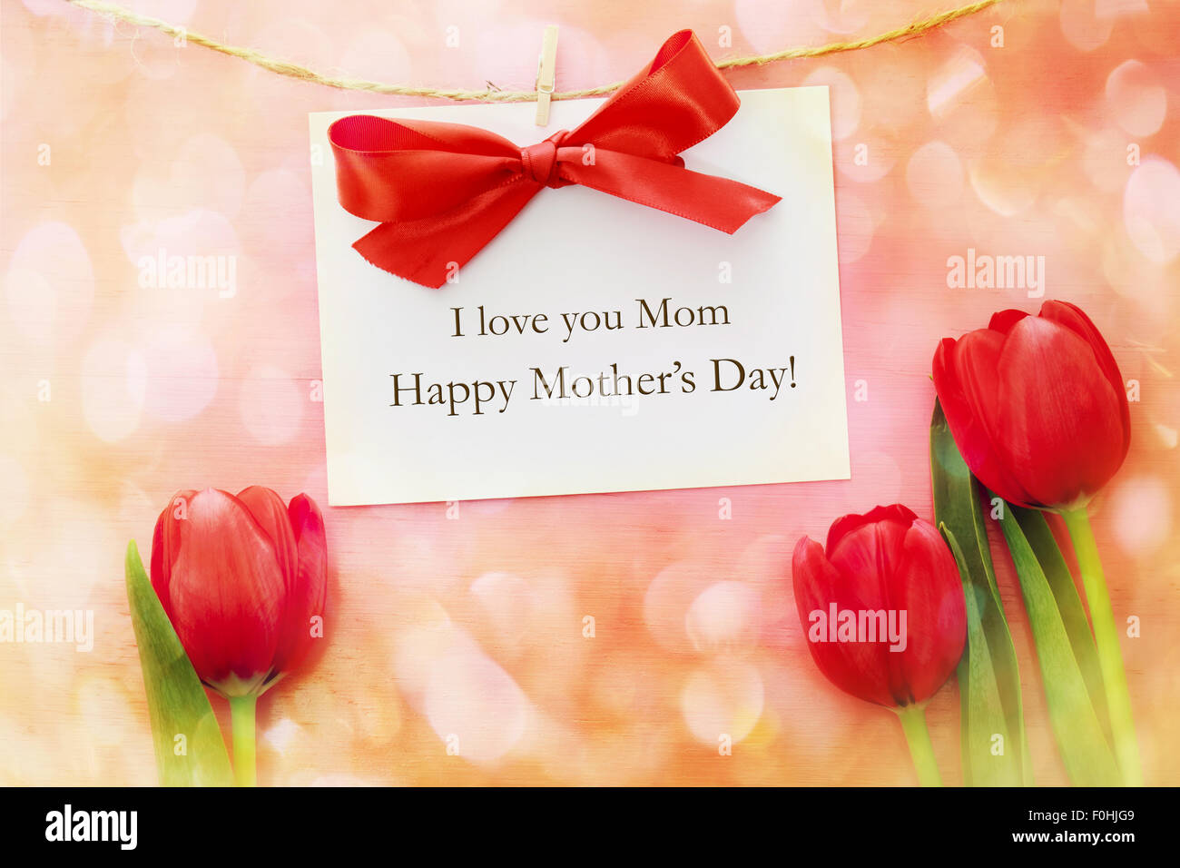 Mütter-Tageskarte über rote Tulpen und rosa Holzbrett mit Wäscheklammern hängen Stockfoto