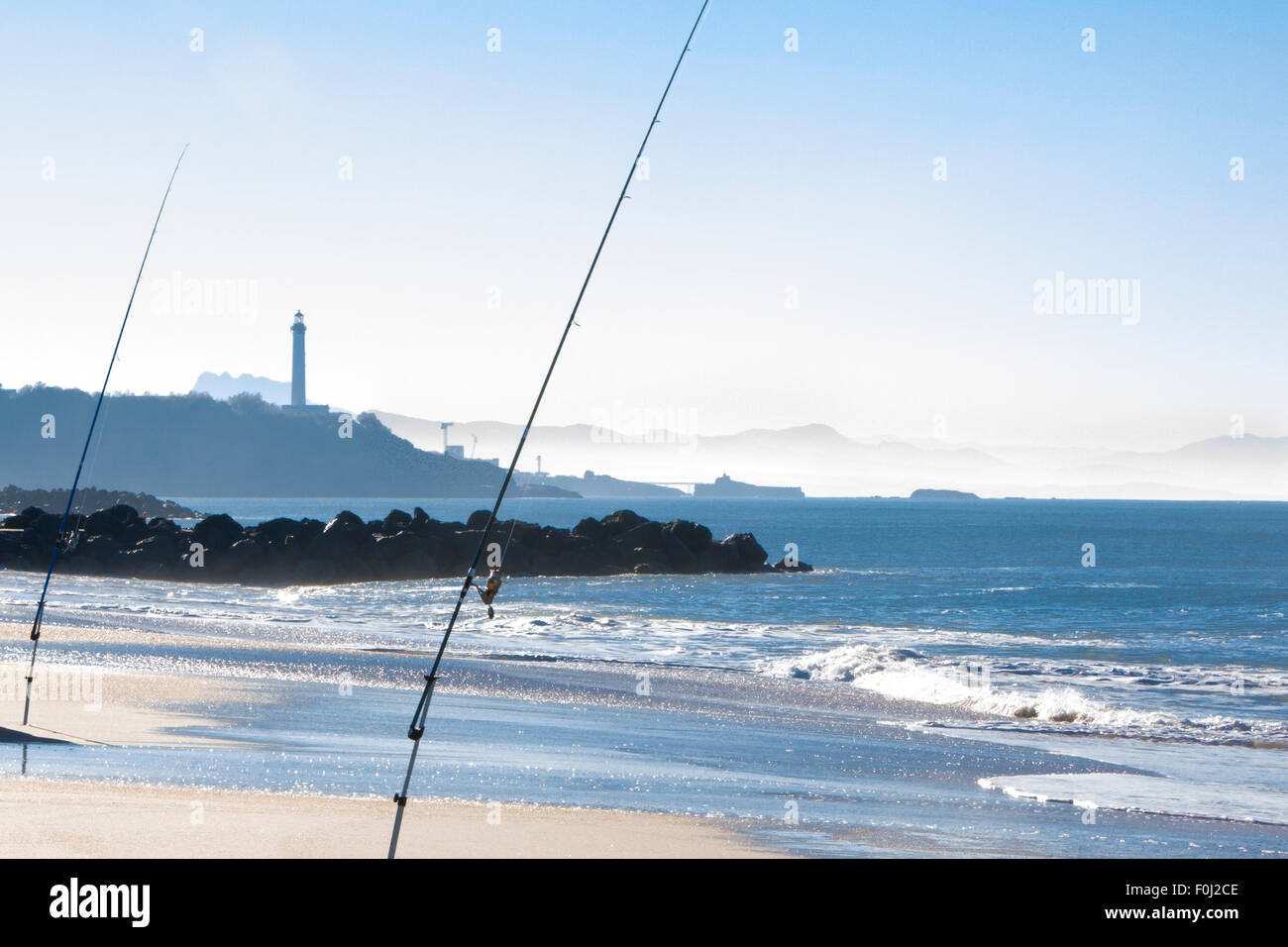 Angelruten in Aktion am frühen Nachmittag auf der Cote Basque in Biarritz mit dem Leuchtturm und dem Strand im Hintergrund. Stockfoto
