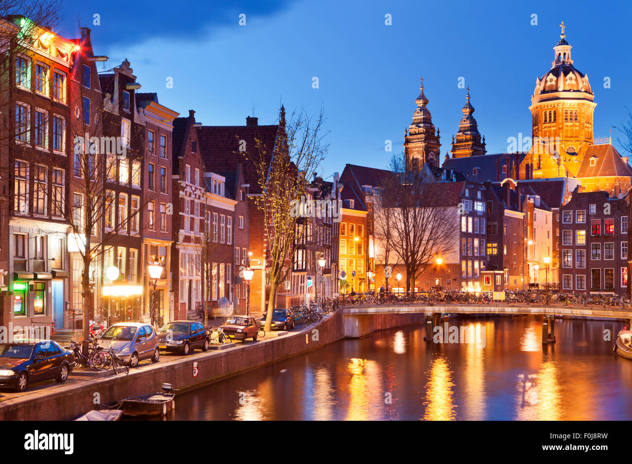 Ein Kanal im Rotlichtviertel in Amsterdam, Die Niederlande mit der St. Nikolaus Kirche am Ende fotografiert in der Nacht. Stockfoto