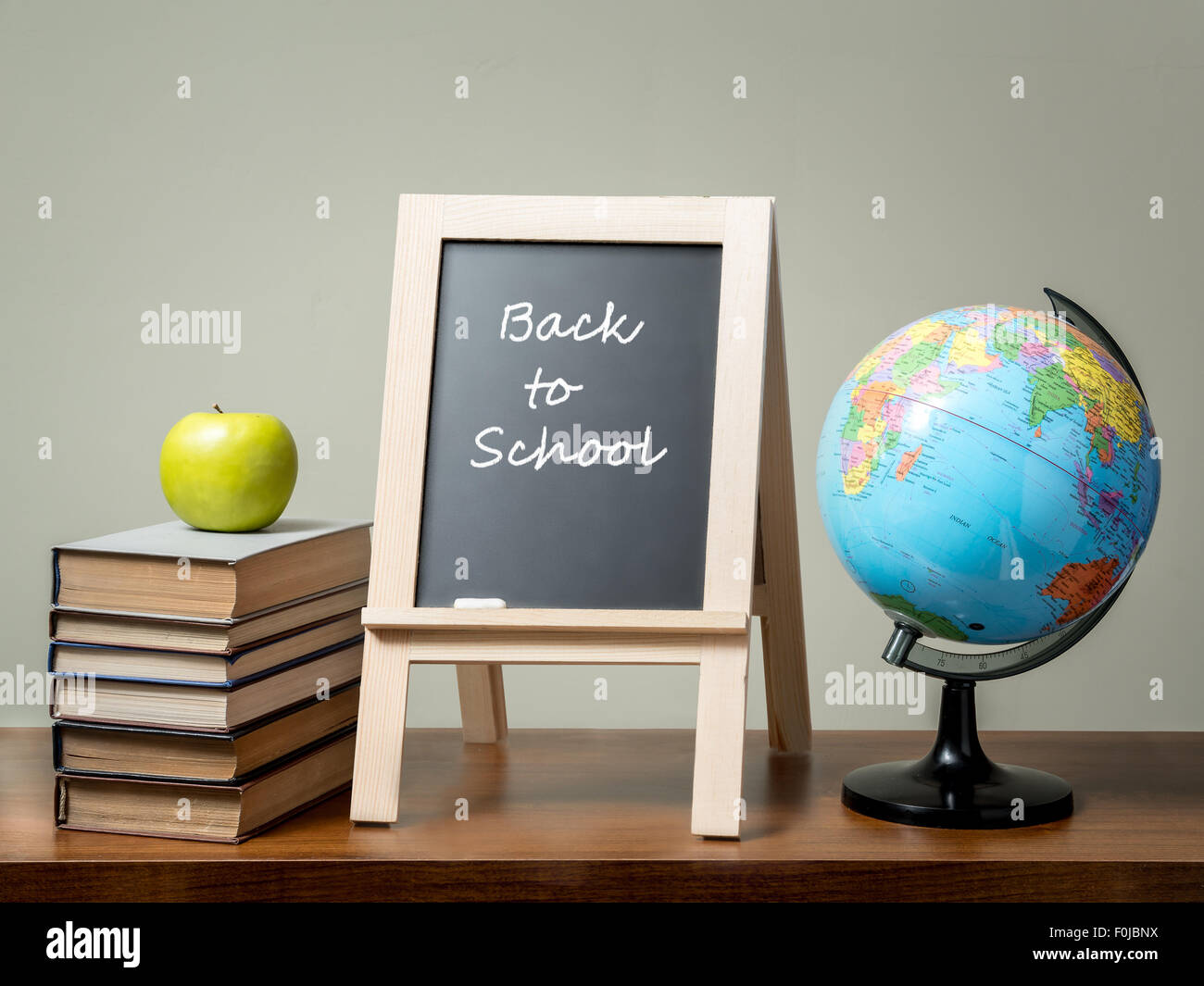 Stapel Bücher mit grünem Apfel, Globe und Tafel mit Back to School Satz alle über grüne Wand auf braunen Schreibtisch gelegt. Stockfoto