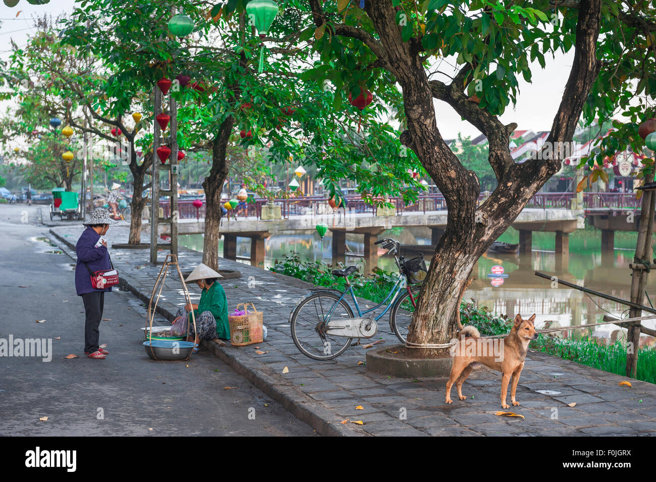 Hoi an Vietnam Street, Blick entlang des Flusses Thu Bon in Hoi an auf einen Straßenverkäufer, der sich mit einem Kunden, Hoi an Old Town, Zentralvietnam, unterhält. Stockfoto