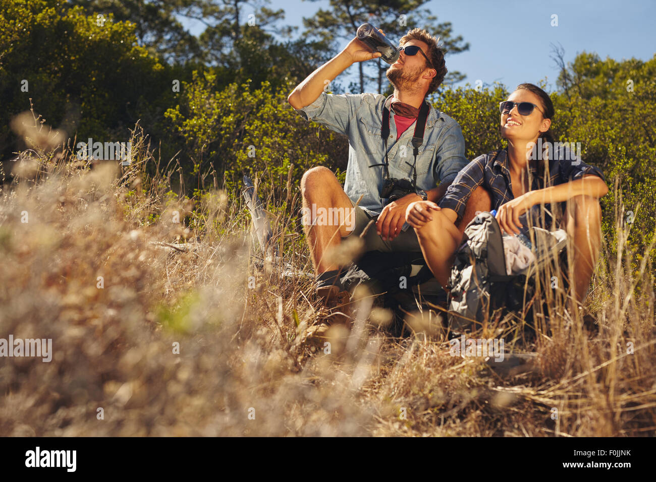 Im Freien Schuss des jungen Paares sitzen gemeinsam eine Pause auf Wanderung. Kaukasischen Mann und Frau Trinkwasser während Sie wandern. Stockfoto