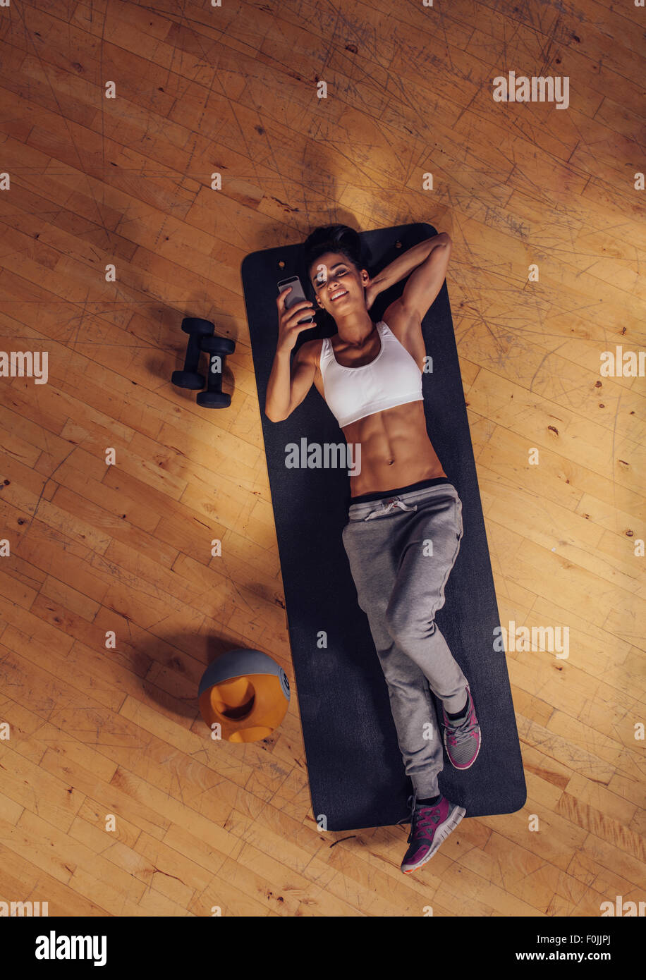 Draufsicht der Frau entspannend auf Yoga-Matte mit Handy. Fitness-Frau eine Pause auf Gymnastikmatte in Turnhalle Te lesen liegend Stockfoto