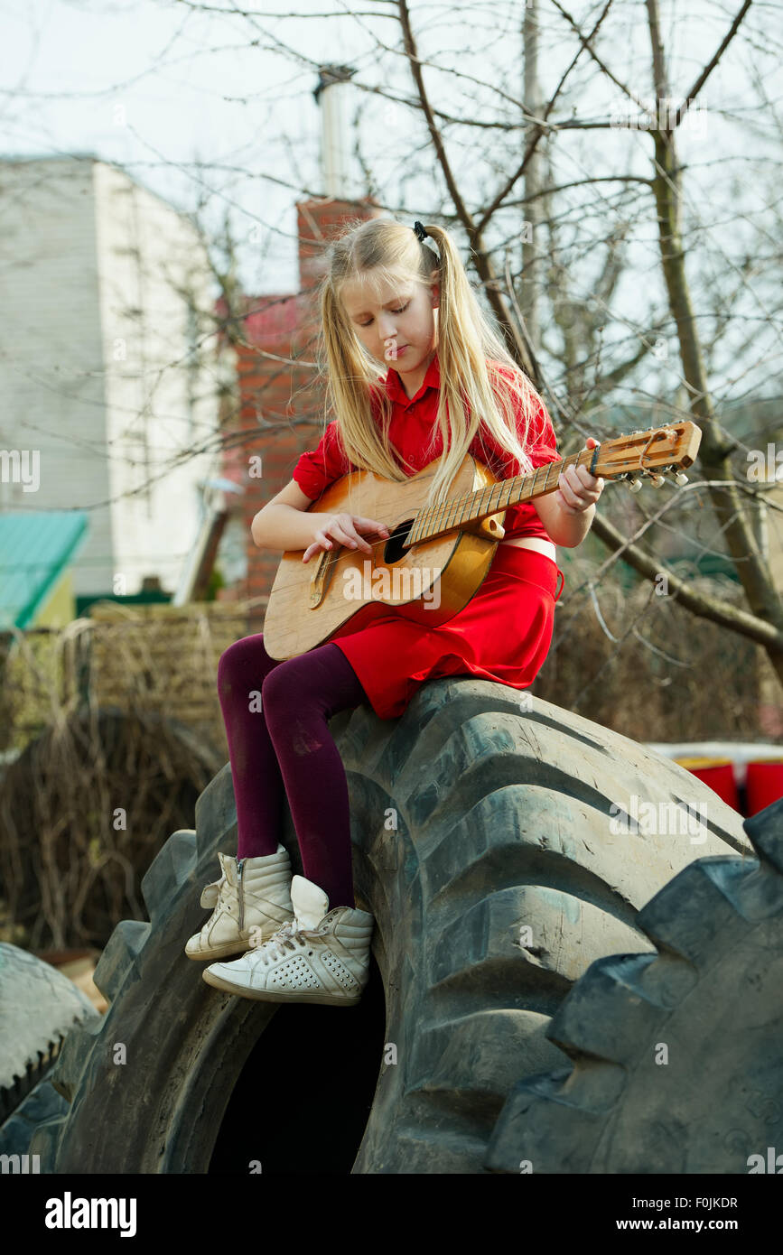 Mädchen spielt Gitarre, sitzend auf Reifen Stockfoto