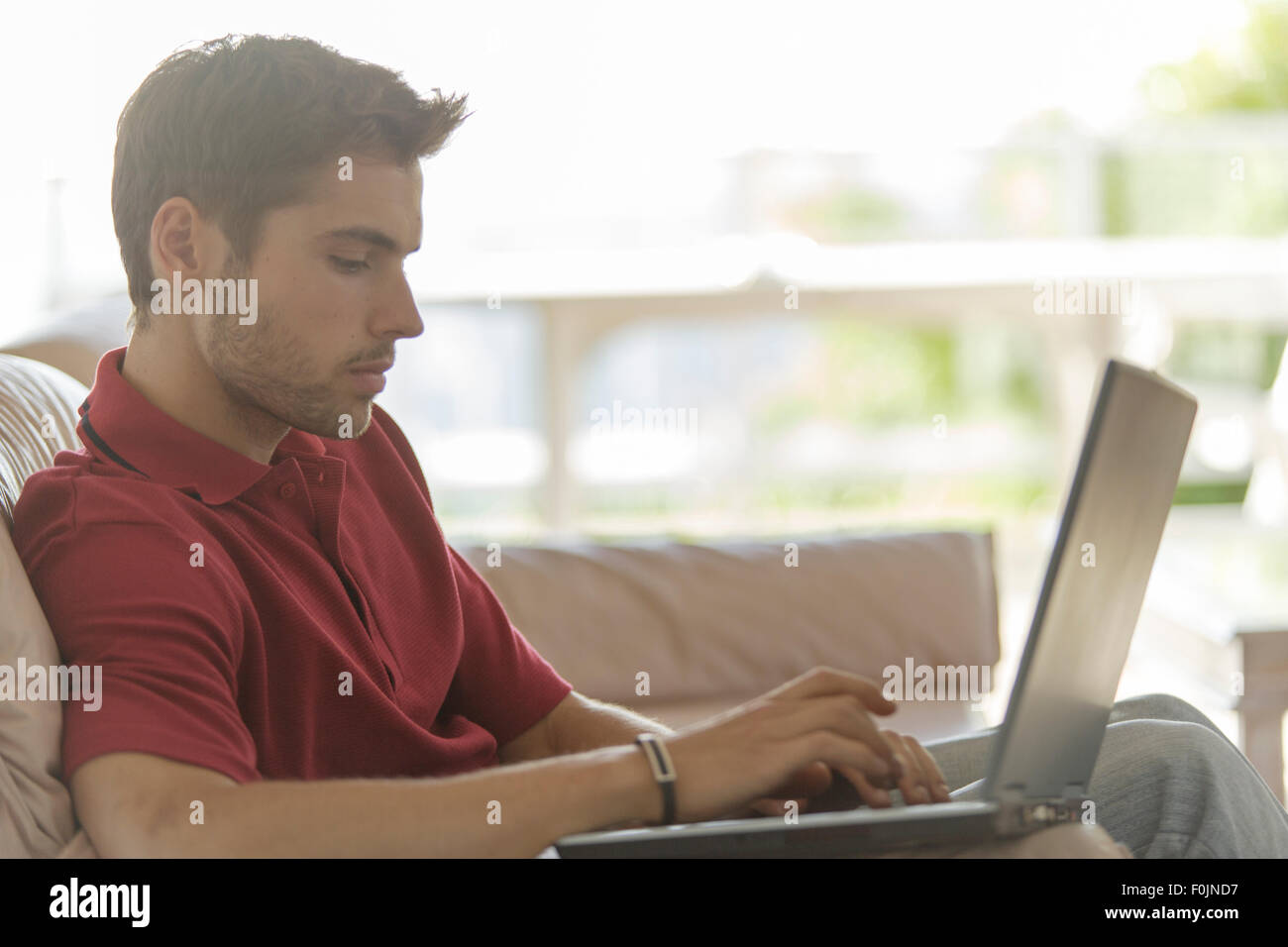 Junger Mann auf der Couch auf Laptop Stockfoto