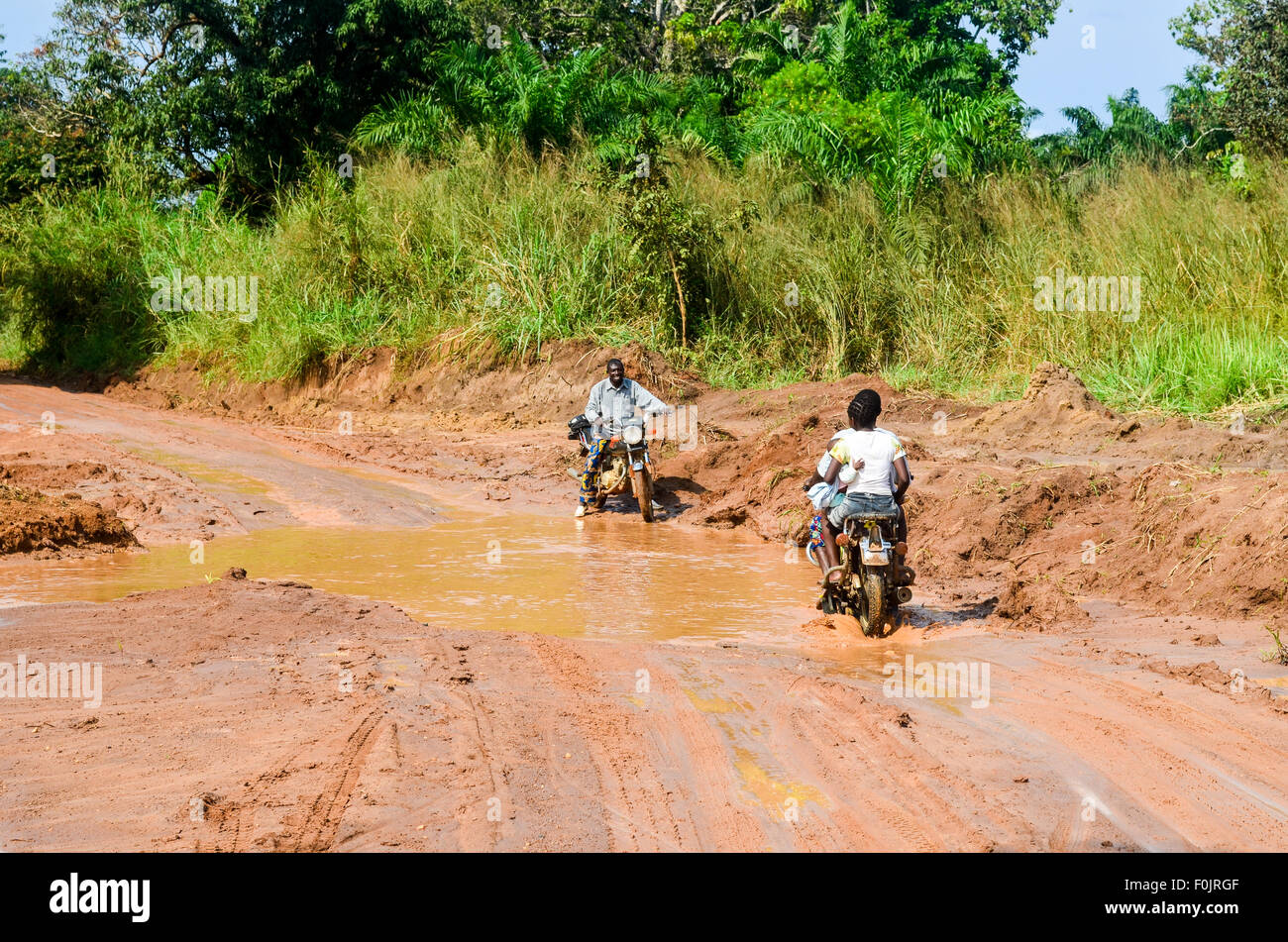 Motorradfahrer auf einem Feldweg überflutet rote Erde in ländlichen Regionen Afrikas Stockfoto